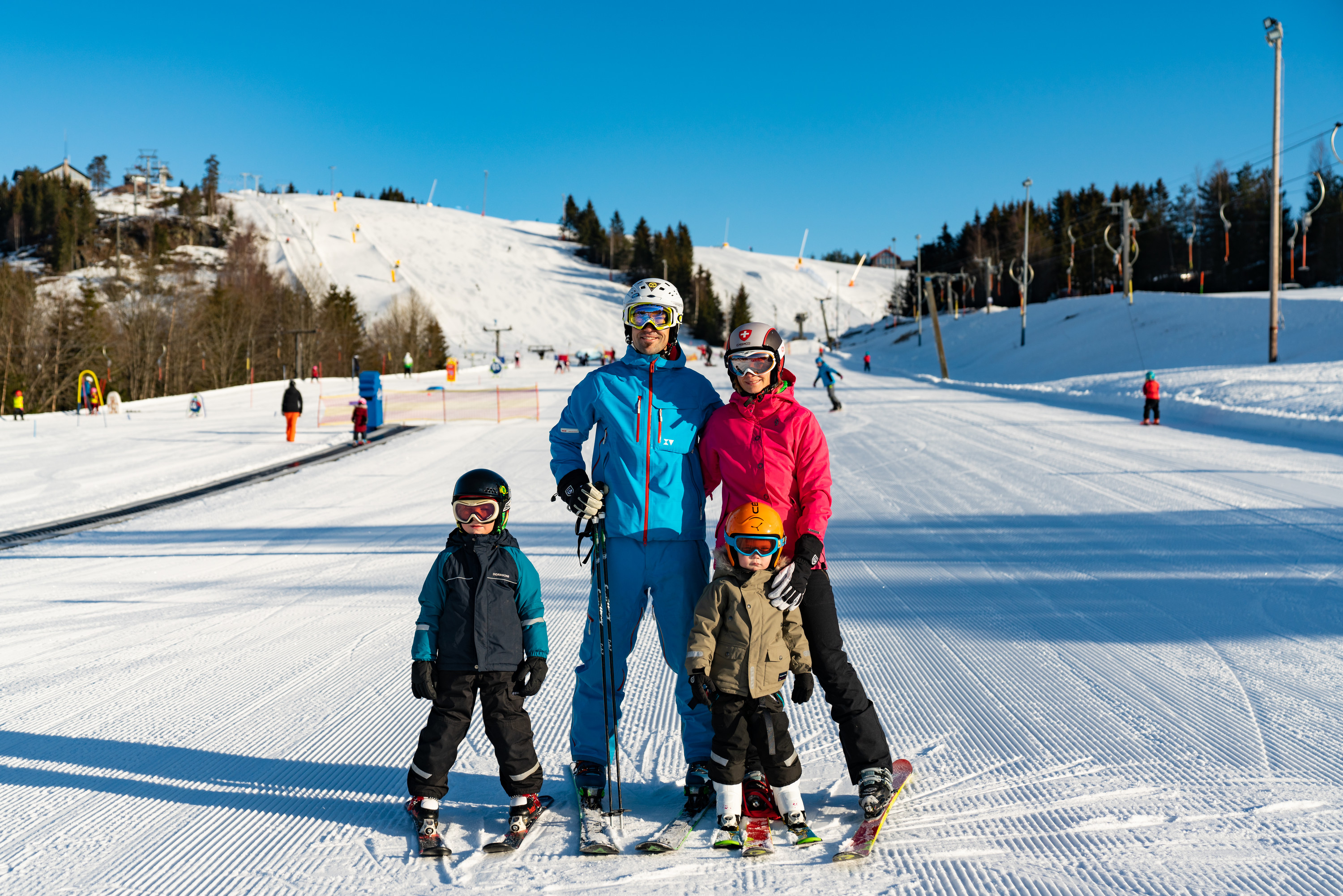 Familj på slalomskidor som står tillsammans nedanför en alpinbacke i Orsa Grönklitt