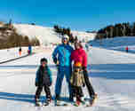 Familj på slalomskidor som står tillsammans nedanför en alpinbacke