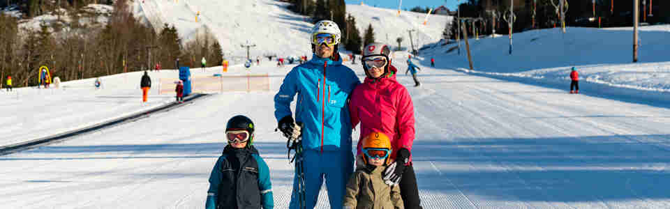Familj på slalomskidor som står tillsammans nedanför en alpinbacke